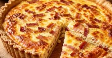 Quiche lorraine dorée dans un moule à tarte, avec une pâte brisée croustillante, une garniture crémeuse aux lardons et du fromage gratiné.