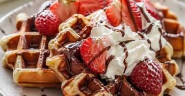 Gaufres maison dorées et croustillantes servies avec chantilly onctueuse, fraises fraîches coupées et filet de sauce chocolat.