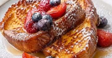 Tranches de pain perdu dorées et moelleuses servies avec des fruits rouges frais, un filet de miel et une légère touche de sucre glace.