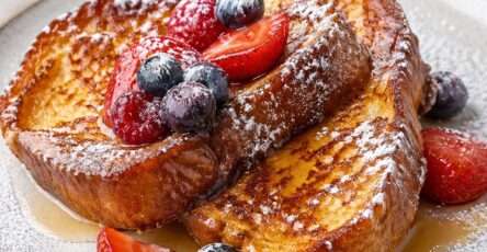 Tranches de pain perdu dorées et moelleuses servies avec des fruits rouges frais, un filet de miel et une légère touche de sucre glace.