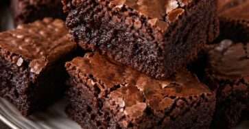 Carrés de brownie au chocolat noir fondant, avec une surface légèrement craquante, des noix visibles et un cœur dense et moelleux.