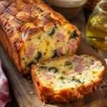 Cake salé jambon fromage olives coupé en tranches, avec une texture moelleuse, une croûte dorée et des morceaux d’olives visibles.