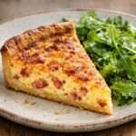 Quiche lorraine traditionnelle dorée, garnie de lardons fumés, servie en parts avec une pâte croustillante et une salade verte.
