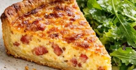 Quiche lorraine traditionnelle dorée, garnie de lardons fumés, servie en parts avec une pâte croustillante et une salade verte.