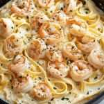 Pâtes Alfredo crémeuses aux crevettes servies dans une assiette creuse, avec sauce au parmesan, ail, persil frais et poivre noir
