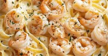 Pâtes Alfredo crémeuses aux crevettes servies dans une assiette creuse, avec sauce au parmesan, ail, persil frais et poivre noir