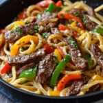 Pâtes au steak et poivron grésillantes servies chaudes, avec lanières de bœuf dorées, poivrons rouges, ail, paprika, persil frais et parmesan
