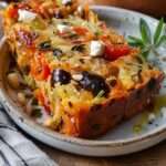 Gâteau salé moelleux aux tomates séchées, feta, olives noires et gruyère râpé, coupé en tranches dorées sur une planche en bois.