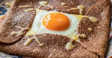 Galette complète bretonne au sarrasin garnie de jambon blanc, fromage râpé fondu et œuf au jaune coulant, pliée en carré.