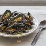 Moules fraîches à la crème liquide, ail haché, beurre, persil frais, poivre noir et sauce onctueuse servies en assiettes creuses.