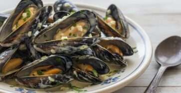 Moules fraîches à la crème liquide, ail haché, beurre, persil frais, poivre noir et sauce onctueuse servies en assiettes creuses.
