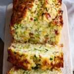 Cake courgette lardons moelleux coupé en tranches, avec fromage râpé, herbes et une texture dorée.