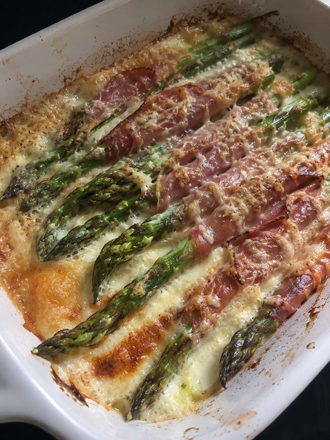 Gratin d’asperges vertes au jambon sec avec crème et fromage gratiné dans un plat rustique doré au four