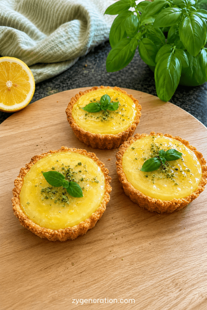 Mini tartelettes au citron maison garnies de crème citron brillante, d’un filet d’huile d’olive douce et de feuilles de basilic frais.