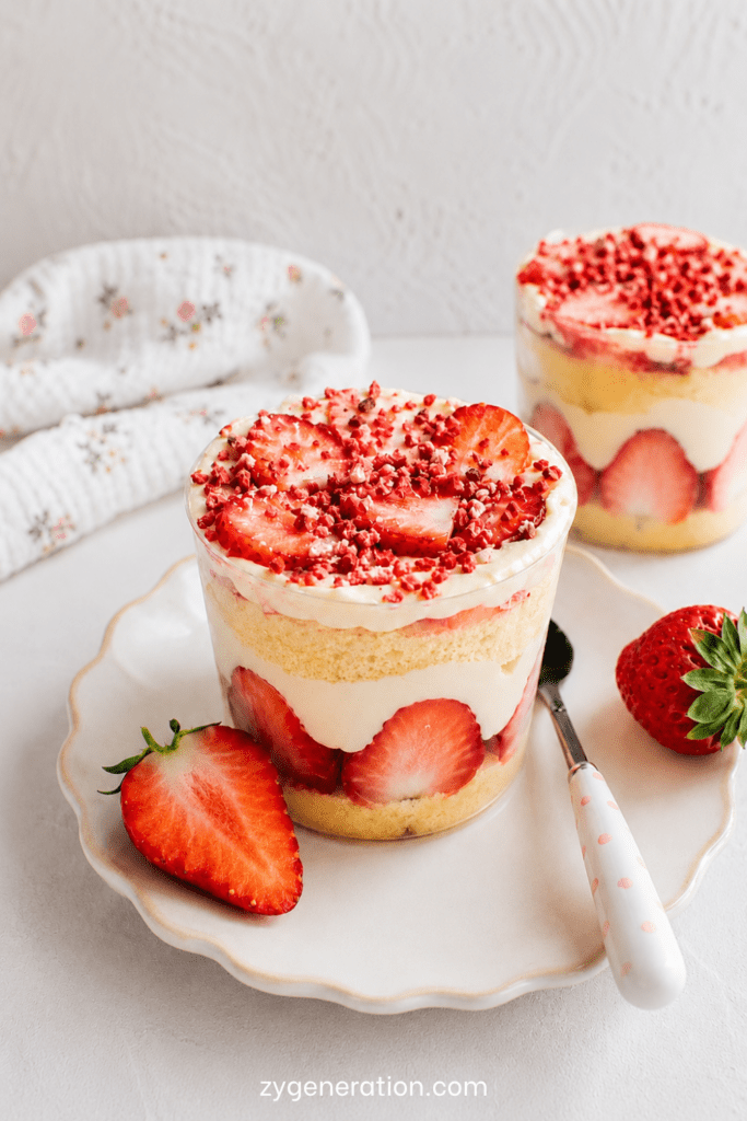 Cup façon fraisier servie dans un verre avec couches de génoise moelleuse, fraises fraîches coupées, crème vanille, chantilly et miettes de fraises séchées.