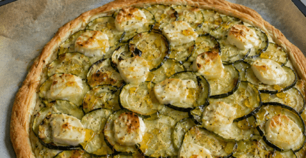 Tarte fine dorée aux courgettes en rondelles, fromage de chèvre fondant, miel brillant, huile d’olive et herbes de Provence sur pâte feuilletée.