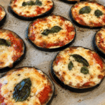 Rondelles épaisses d’aubergines façon pizza gratinées au four avec sauce tomate, mozzarella fondue, origan et feuilles de basilic frais.