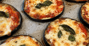Rondelles épaisses d’aubergines façon pizza gratinées au four avec sauce tomate, mozzarella fondue, origan et feuilles de basilic frais.