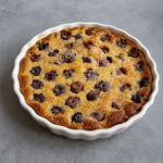 Clafoutis maison aux cerises et aux amandes doré au four, servi dans un plat à gratin avec une texture moelleuse et des cerises visibles.