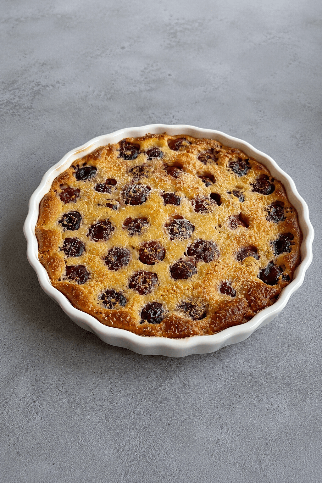 Clafoutis maison aux cerises et aux amandes doré au four, servi dans un plat à gratin avec une texture moelleuse et des cerises visibles.