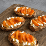 Bruschettas dorées garnies de fromage de chèvre frais, fines tranches d’abricots, filet de miel et poivre sur pain grillé.