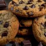 Cookies aux pépites de chocolat noir faits maison, dorés sur les bords et moelleux au centre, servis sur une assiette avec quelques pépites fondantes.