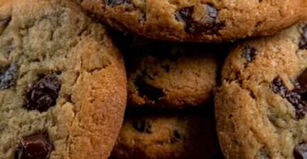 Cookies aux pépites de chocolat noir faits maison, dorés sur les bords et moelleux au centre, servis sur une assiette avec quelques pépites fondantes.