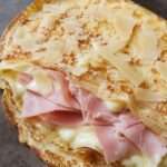 Crêpe savoyarde dorée garnie de jambon blanc, fromage fondant, crème fraîche et copeaux de parmesan, servie chaude dans une assiette.