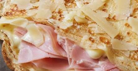 Crêpe savoyarde dorée garnie de jambon blanc, fromage fondant, crème fraîche et copeaux de parmesan, servie chaude dans une assiette.