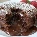 Fondant au chocolat individuel avec cœur coulant, saupoudré de sucre glace et décoré de fraises fraîches dans une assiette de dessert.