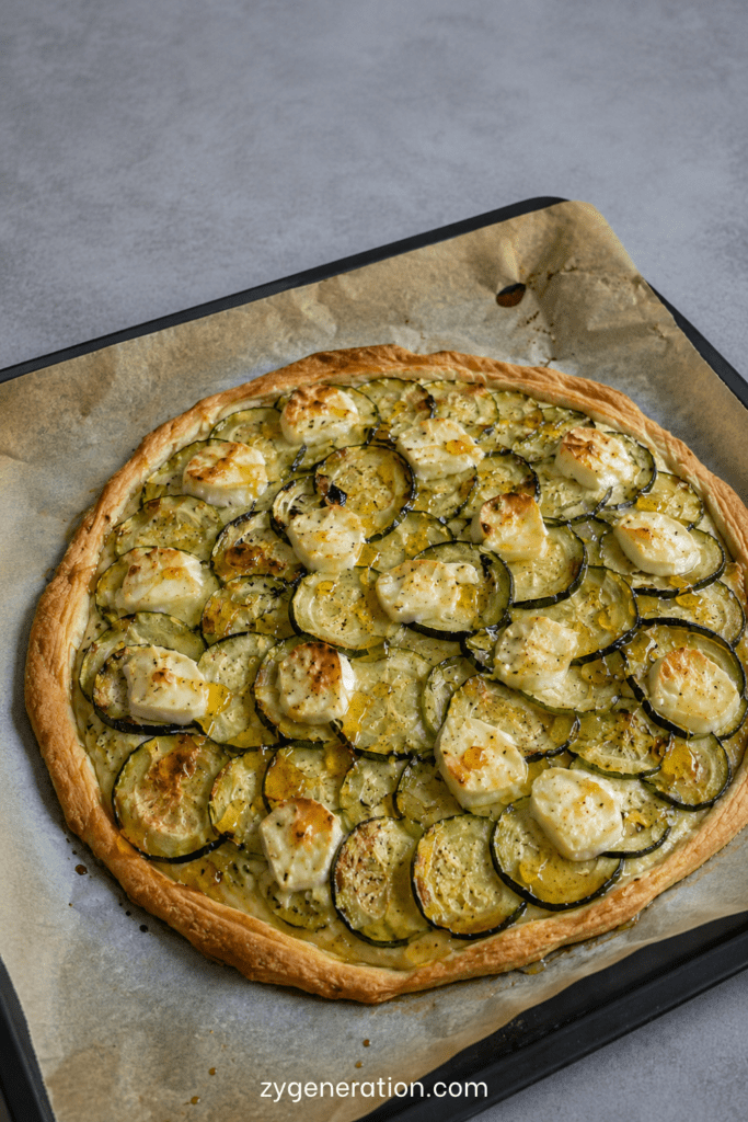 Tarte fine dorée aux courgettes en rondelles, fromage de chèvre fondant, miel brillant, huile d’olive et herbes de Provence sur pâte feuilletée.