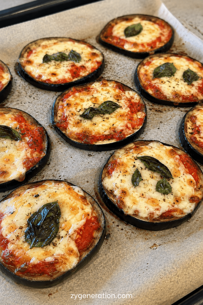 Rondelles épaisses d’aubergines façon pizza gratinées au four avec sauce tomate, mozzarella fondue, origan et feuilles de basilic frais.