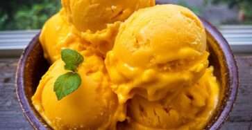 Boules de glace à la mangue maison servies dans une coupe, avec une texture crémeuse jaune doré et une feuille de menthe fraîche en décoration.