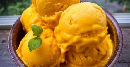 Boules de glace à la mangue maison servies dans une coupe, avec une texture crémeuse jaune doré et une feuille de menthe fraîche en décoration.