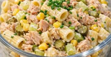 Salade froide de pâtes au thon servie dans un saladier, avec maïs, céleri croquant, cornichons, ciboulette et sauce crémeuse au yaourt.