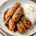Boulettes de poulet japonaises façon tsukune, brillantes et caramélisées dans une sauce soja au miel, servies avec du riz blanc et des graines de sésame.