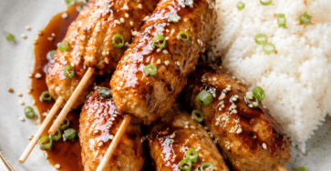 Boulettes de poulet japonaises façon tsukune, brillantes et caramélisées dans une sauce soja au miel, servies avec du riz blanc et des graines de sésame.