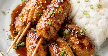 Boulettes de poulet japonaises façon tsukune, brillantes et caramélisées dans une sauce soja au miel, servies avec du riz blanc et des graines de sésame.