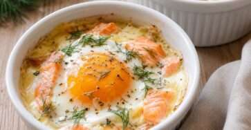 Quatre ramequins d’œufs cocotte au saumon fumé, à la crème et au fromage, cuits au bain-marie et garnis d’aneth frais.