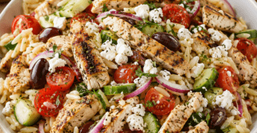 Salade d’orzo au poulet à la grecque présenté dans une vaisselle claire, avec les ingrédients principaux visibles et une lumière naturelle chaude