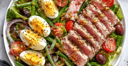 Salade niçoise moderne composée de tranches de thon grillé rosé, d’œufs durs, de tomates fraîches, de haricots verts croquants et d’olives noires, servie dans une grande assiette avec une vinaigrette à la moutarde.