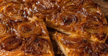 Tarte Tatin salée aux oignons caramélisés, retournée sur une assiette, avec une surface brillante et dorée, une pâte feuilletée croustillante et quelques brins de thym frais.