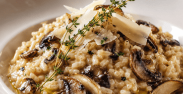 Risotto crémeux aux champignons servi dans une assiette creuse, garni de champignons dorés, de parmesan râpé, de persil frais et de quelques gouttes d’huile de truffe.