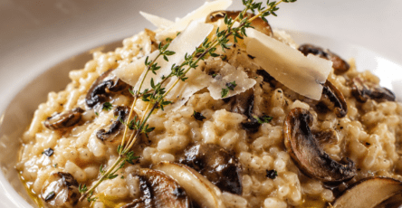 Risotto crémeux aux champignons servi dans une assiette creuse, garni de champignons dorés, de parmesan râpé, de persil frais et de quelques gouttes d’huile de truffe.