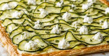 Tarte fine rectangulaire en pâte feuilletée garnie de ricotta et de fines rondelles de courgettes disposées en écailles, dorées sur les bords et parfumées aux herbes.
