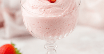 Mousse à la fraise rose pâle servie dans des verrines, à la texture très aérienne, décorée de fraises fraîches et de quelques copeaux de fruit.