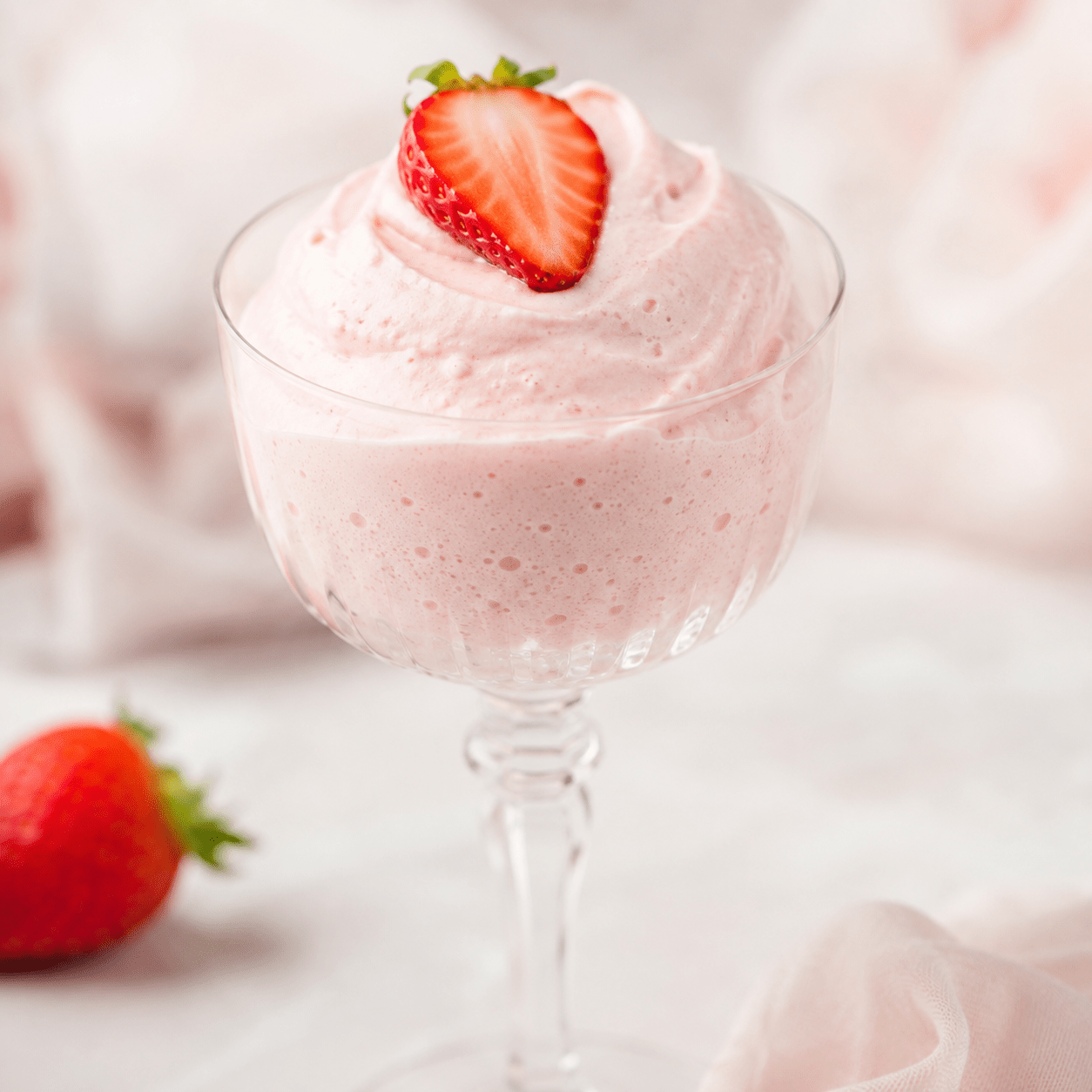 Mousse à la fraise rose pâle servie dans des verrines, à la texture très aérienne, décorée de fraises fraîches et de quelques copeaux de fruit.